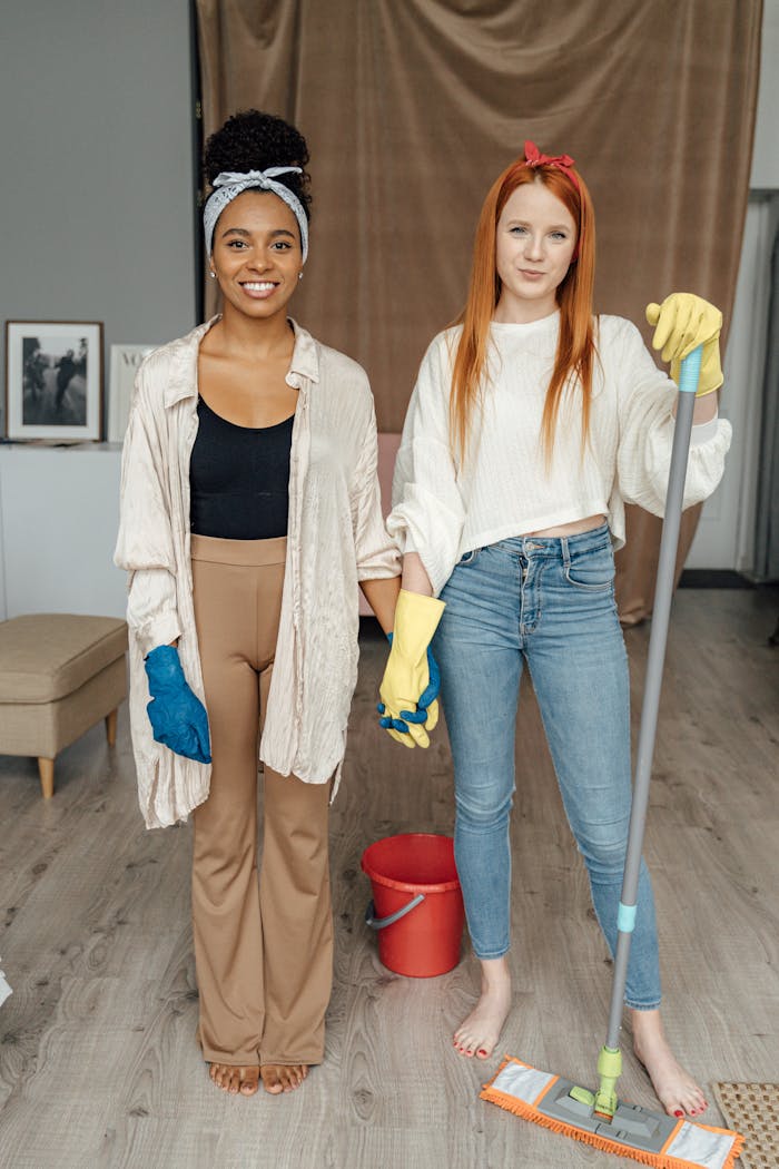 about-02 Two women smiling and holding hands while cleaning indoors, symbolizing teamwork.